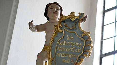 Eine Engelsfigur über einem Beichtstuhl hält eine Tafel mit dem Buß-Psalm "Ich will meine Missethat anzeigen".