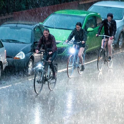 22.04.2018, Niedersachsen, Göttingen: Radfahrer fahren bei kurzzeitigem Starkregen und Gewitter an geparkten Autos vorbei.