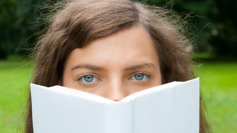 Frau schaut einen über ein Buch hinweg an.