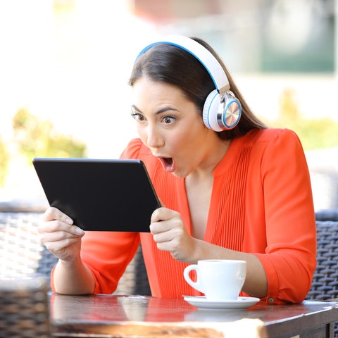 Schockierte Frau blickt auf ein Tablet.