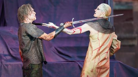 Die blutverschmierten Schauspieler mit jeweils einem Schwert Franz Pätzold (l.) als Dietrich von Bern und Marta Kizyma als Witta in "Der Diplomat" bei den Nibelungenfestspielen Worms 2024